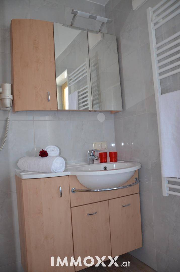 Helles Badezimmer mit Holzschränken, ovalem Waschbecken und einem Spiegelschrank über dem Waschtisch.
