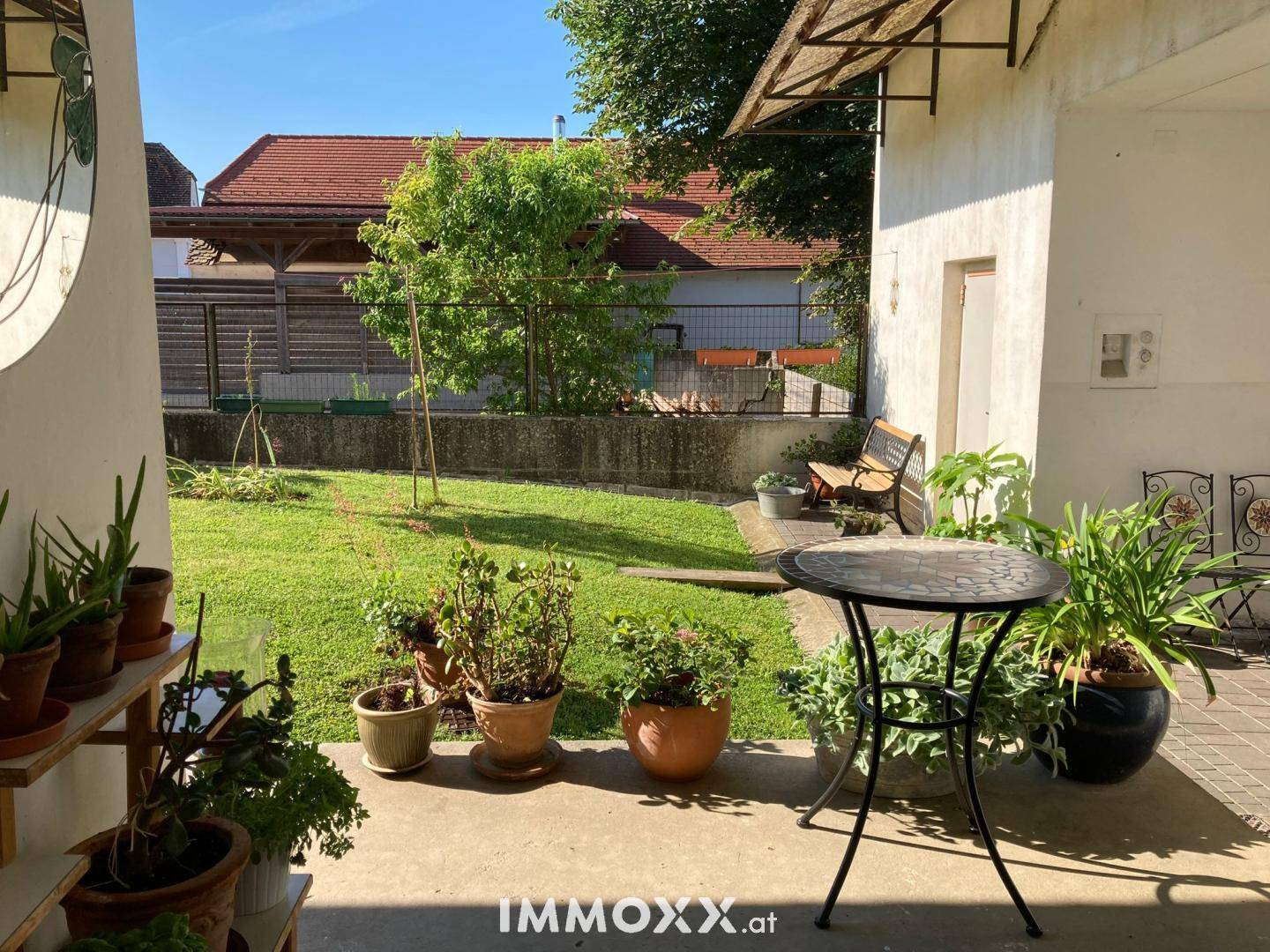 Sonniger Gartenbereich mit Rasenfläche, Topfpflanzen und einem kleinen Terrassentisch.