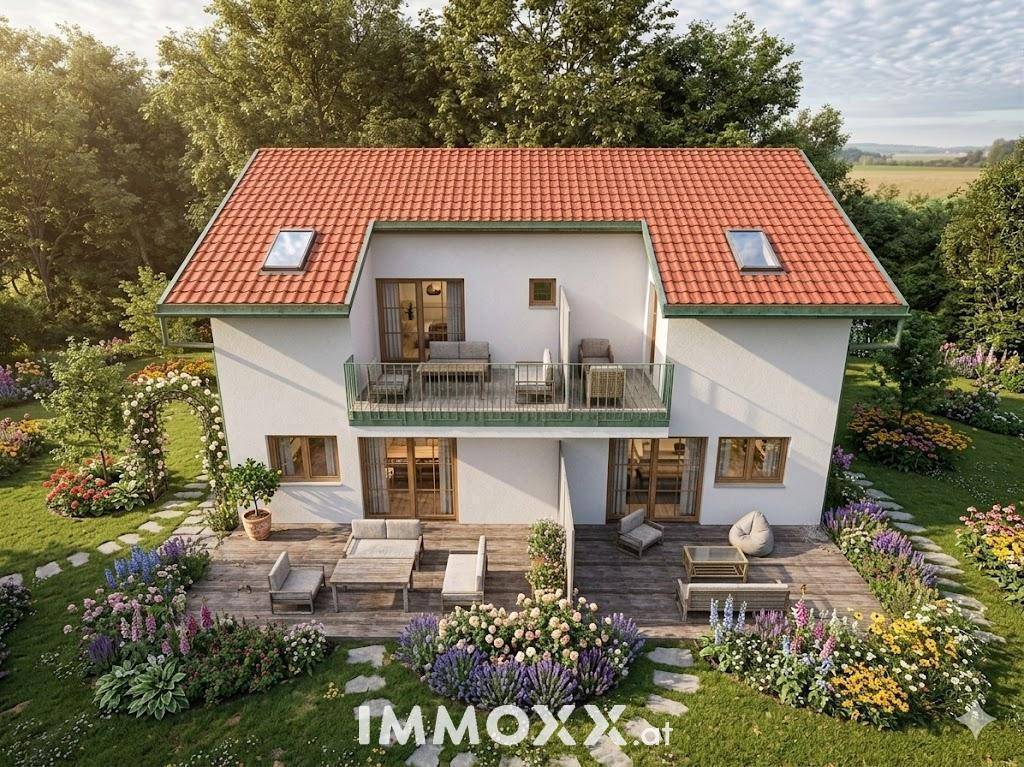 Rückansicht des Hauses mit großer Holzterrasse, Gartenmöbeln und blühenden Blumenbeeten.