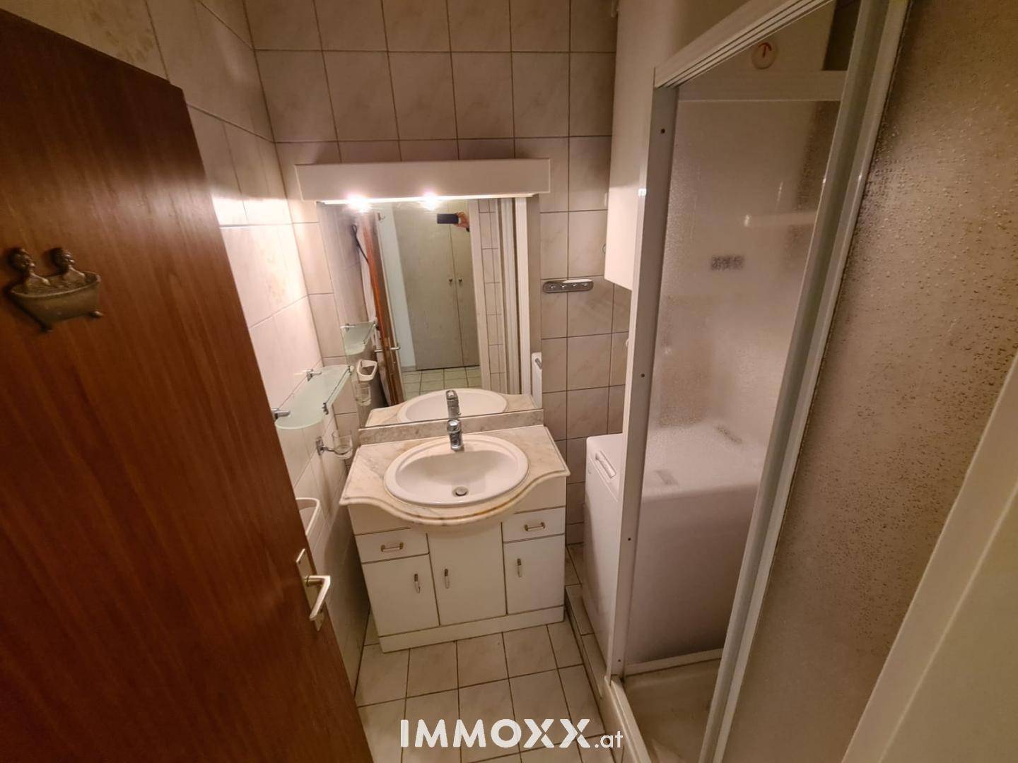 Kleines Badezimmer mit Dusche, Waschbecken und integrierter Waschmaschine.