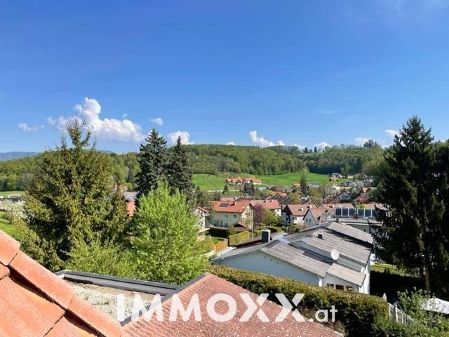 Panoramablick über eine Wohnsiedlung mit grünen Dächern und bewaldeten Hügeln im Hintergrund.