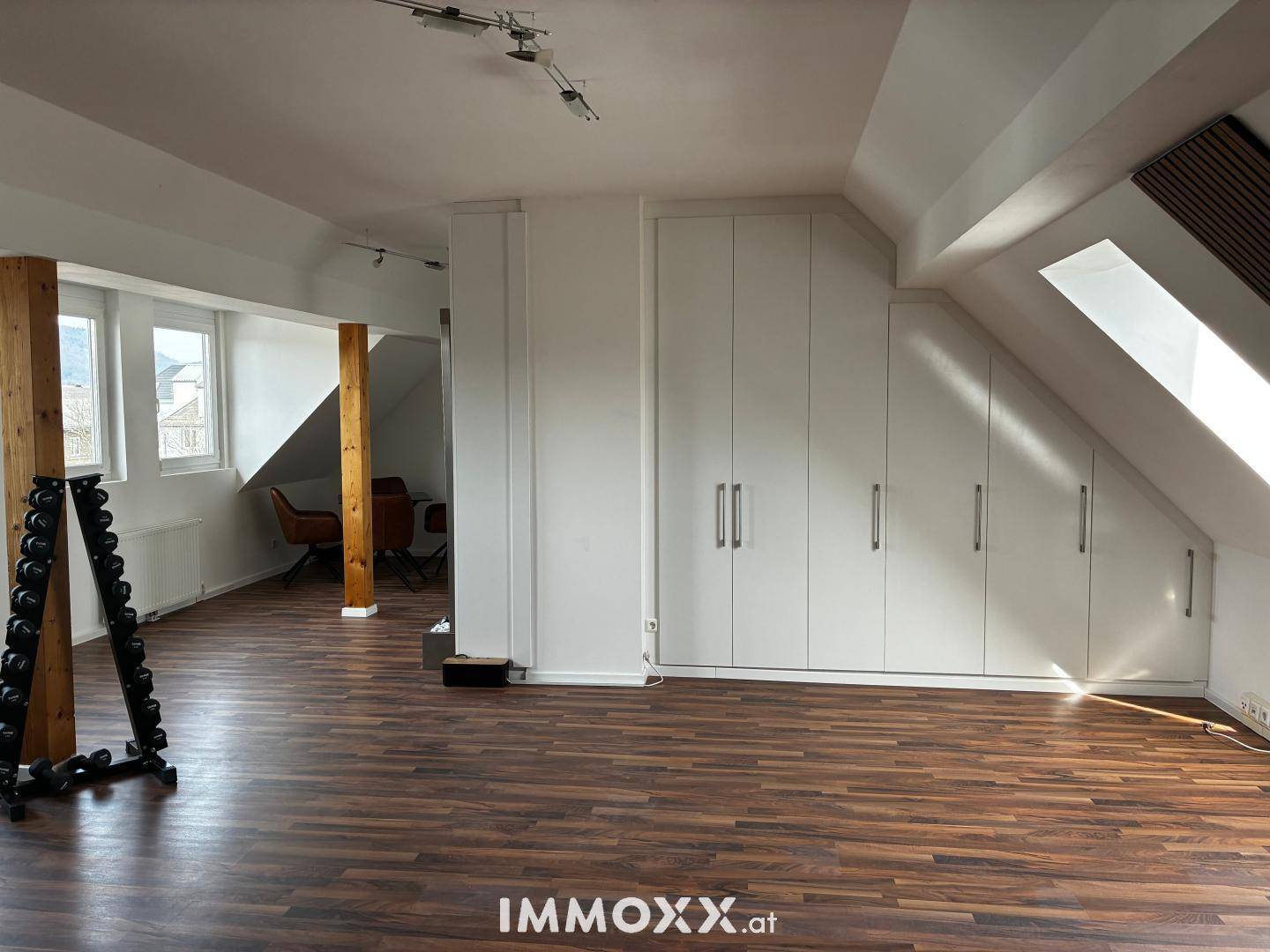 Heller Dachgeschossraum mit maßgefertigten Einbauschränken, Dachfenster und Blick auf einen weiteren Bereich.