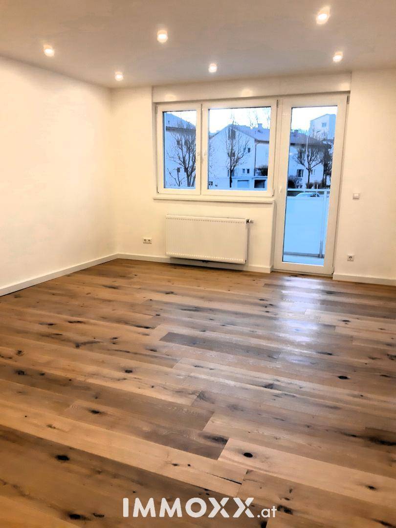 Helles Zimmer mit großem Fenster und Zugang zu einem französischen Balkon, ausgestattet mit Holzfußboden.