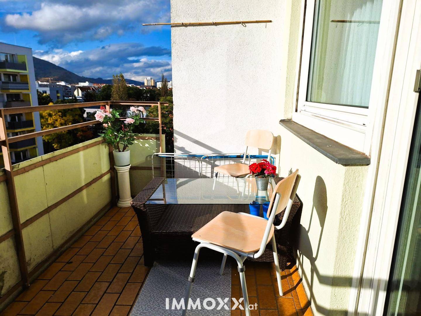 Sonniger Balkon mit Sitzgelegenheiten und Blick auf die Stadt und Berge.