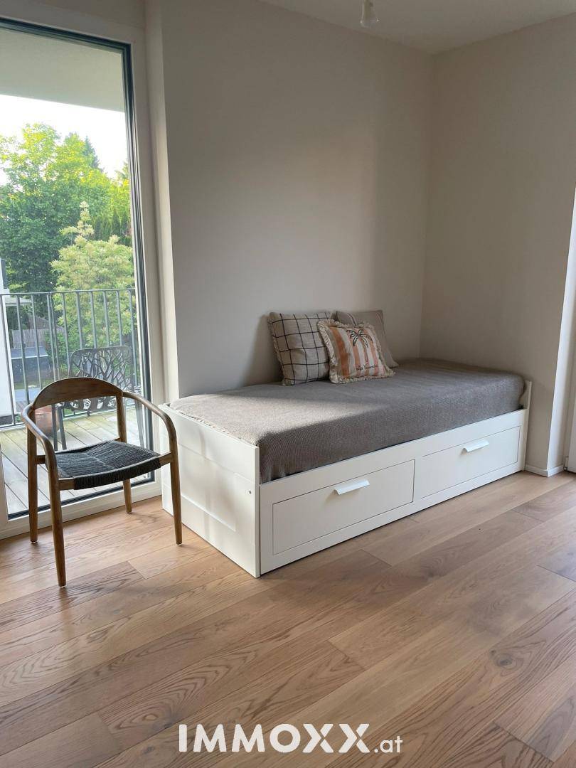 Helles Schlafzimmer mit weißem Tagesbett, Holzboden und direktem Zugang zum sonnigen Balkon.
