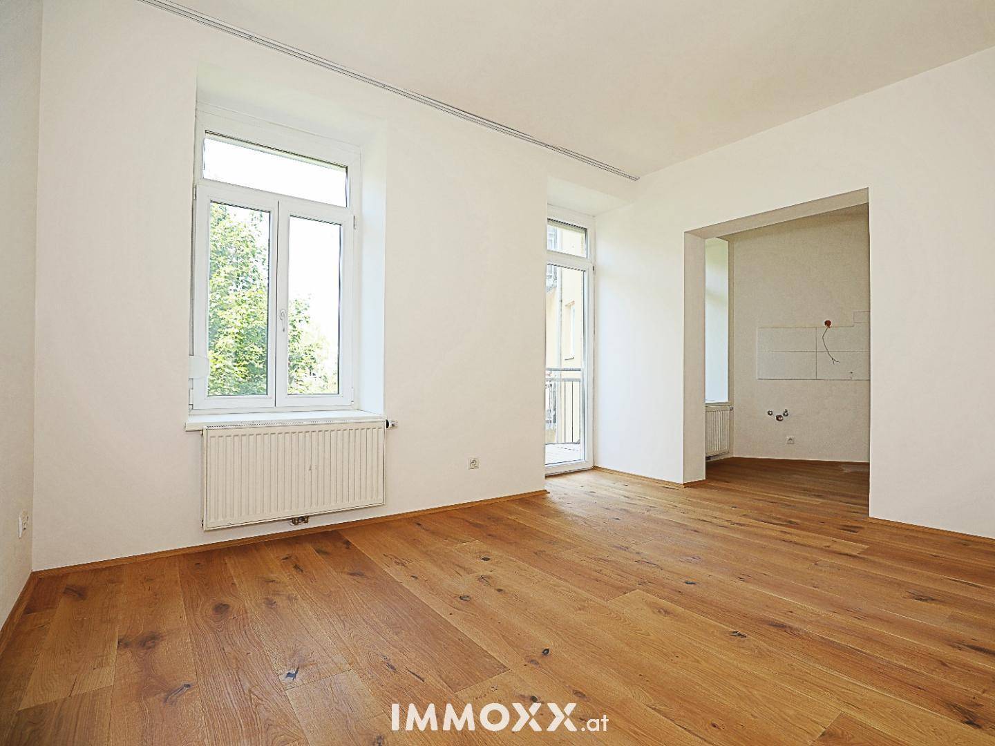 Heller Raum mit Holzboden und Zugang zu einem Balkon, der viel Licht hereinlässt.