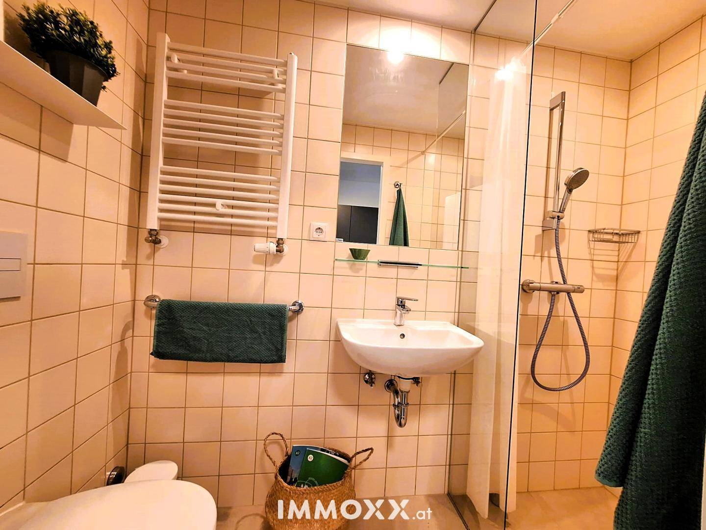 Funktionales Badezimmer mit beigen Fliesen, Dusche und beheiztem Handtuchhalter.