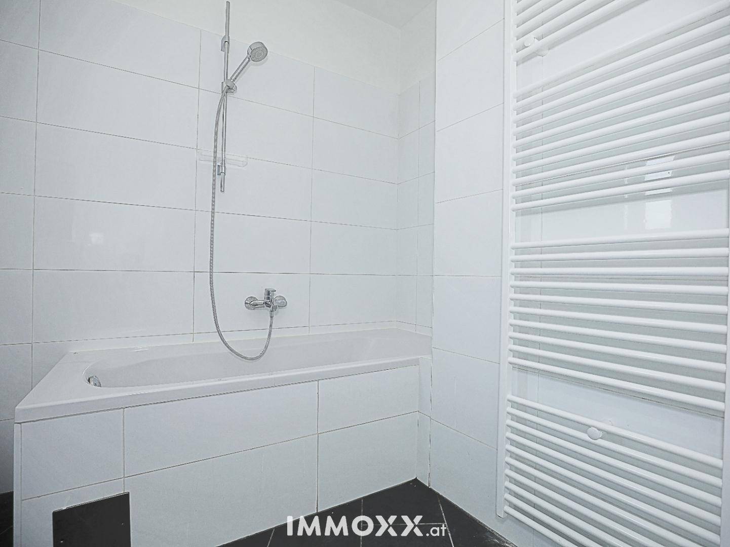 Modern gefliestes Badezimmer mit Badewanne und Duscharmatur sowie einem beheizten Handtuchhalter.