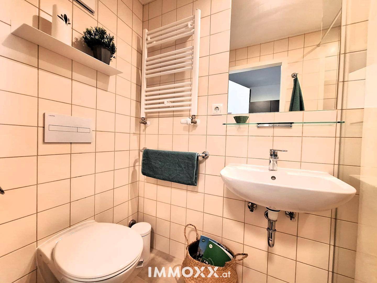 Modernes Badezimmer mit Fliesen, Waschbecken, Toilette und beheiztem Handtuchhalter.