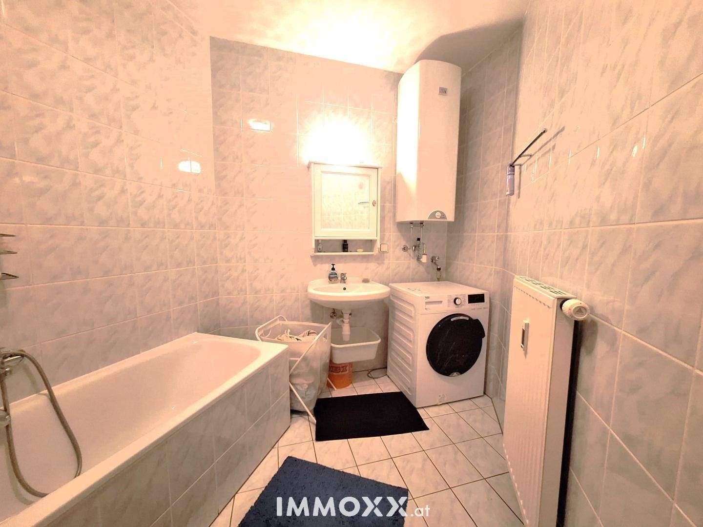 Gefliestes Badezimmer mit Badewanne, Waschbecken, Spiegelschrank und Waschmaschine.