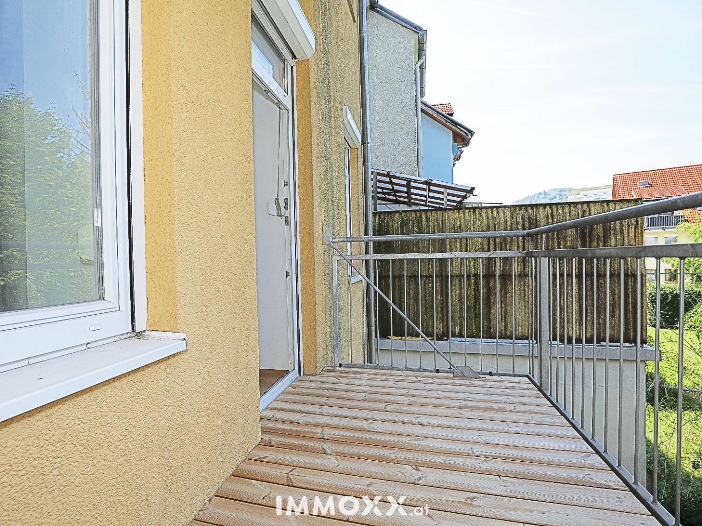 Balkon mit Holzbelag und Metallgeländer, bietet einen seitlichen Blick auf die Nachbarschaft.