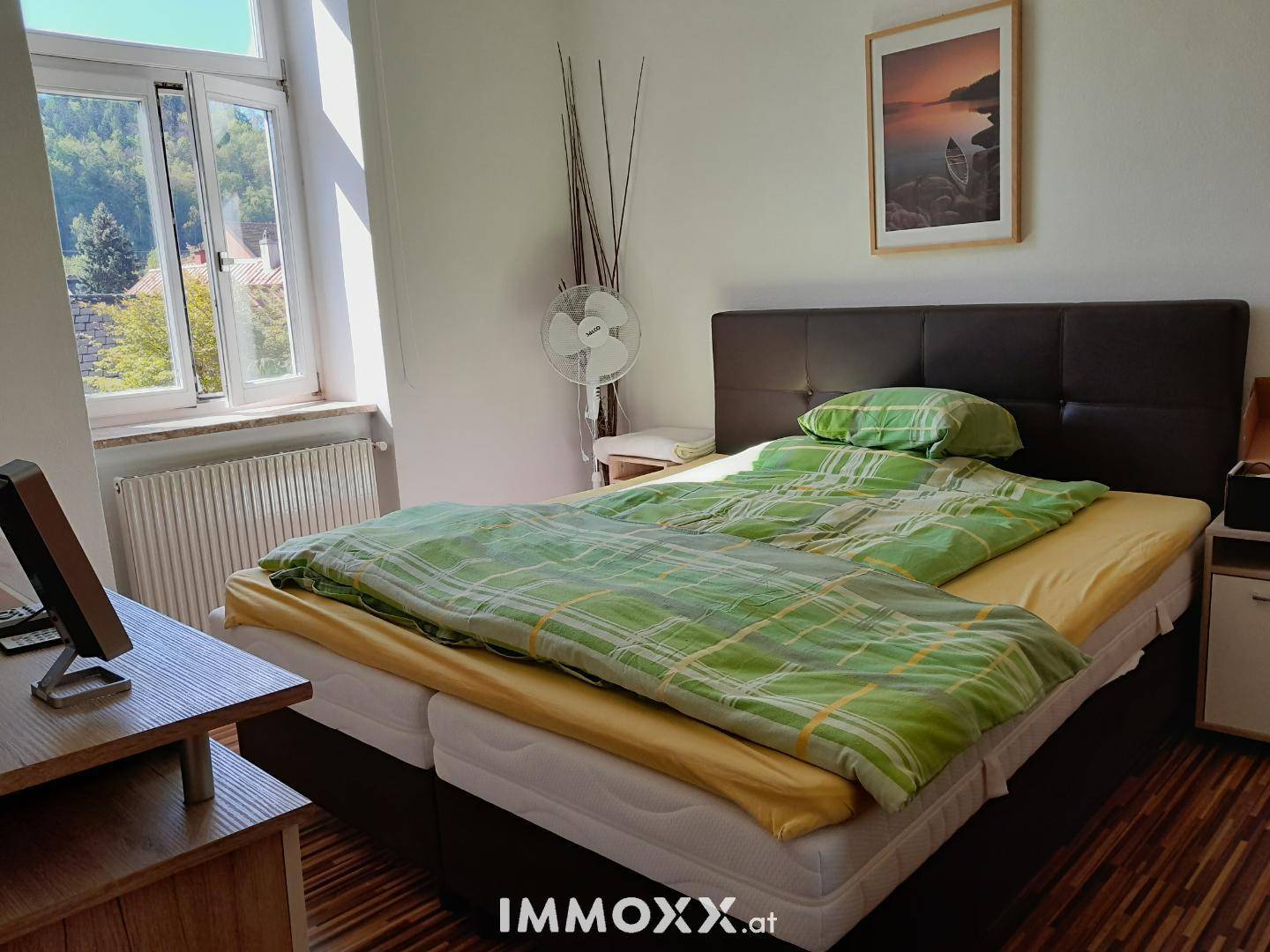 Helles Schlafzimmer mit Doppelbett, Holzfußboden und Blick ins Grüne.