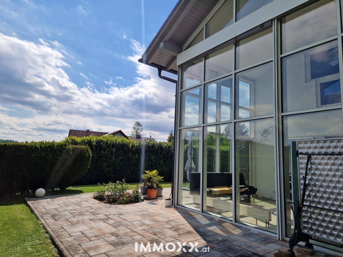 Seitenansicht des modernen Hauses mit großer Glasfront, Wintergarten und gepflasterter Terrasse.