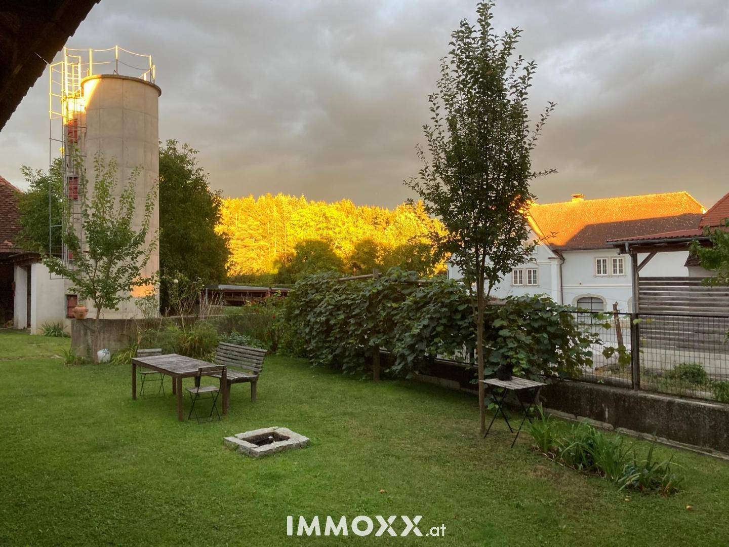 Großer Garten mit Rasenfläche, Bäumen, einem Sitzbereich und einer Feuerstelle.