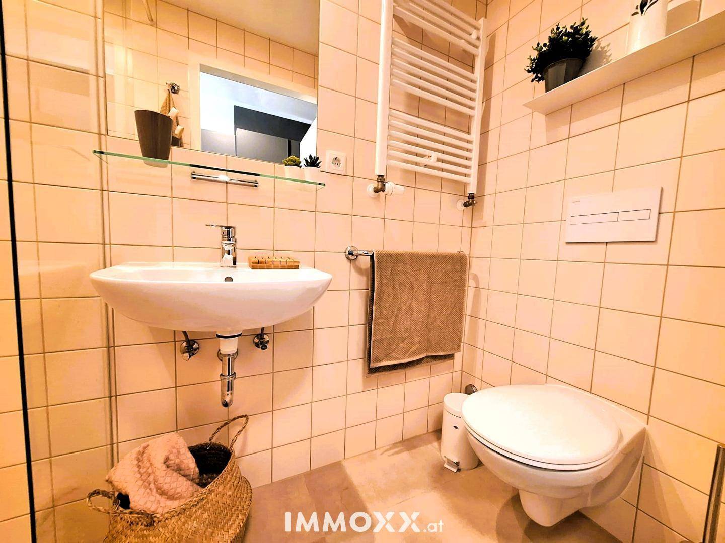 Modernes Badezimmer mit Fliesen, Waschbecken, Toilette und beheiztem Handtuchhalter.