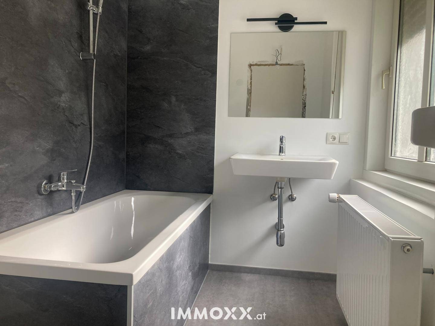 Modernes Badezimmer mit Badewanne, Waschbecken und dunklen Schieferfliesen an den Wänden.