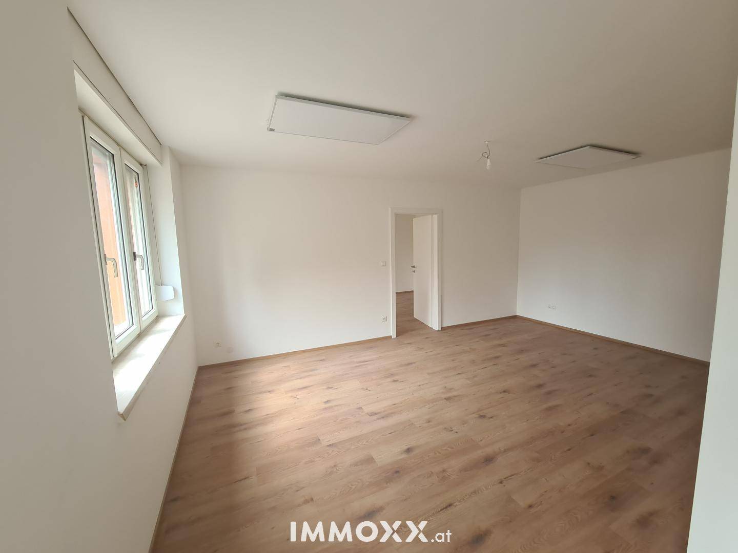Großzügiges Zimmer mit Laminatboden und weiß gestrichenen Wänden, bereit für die Einrichtung.