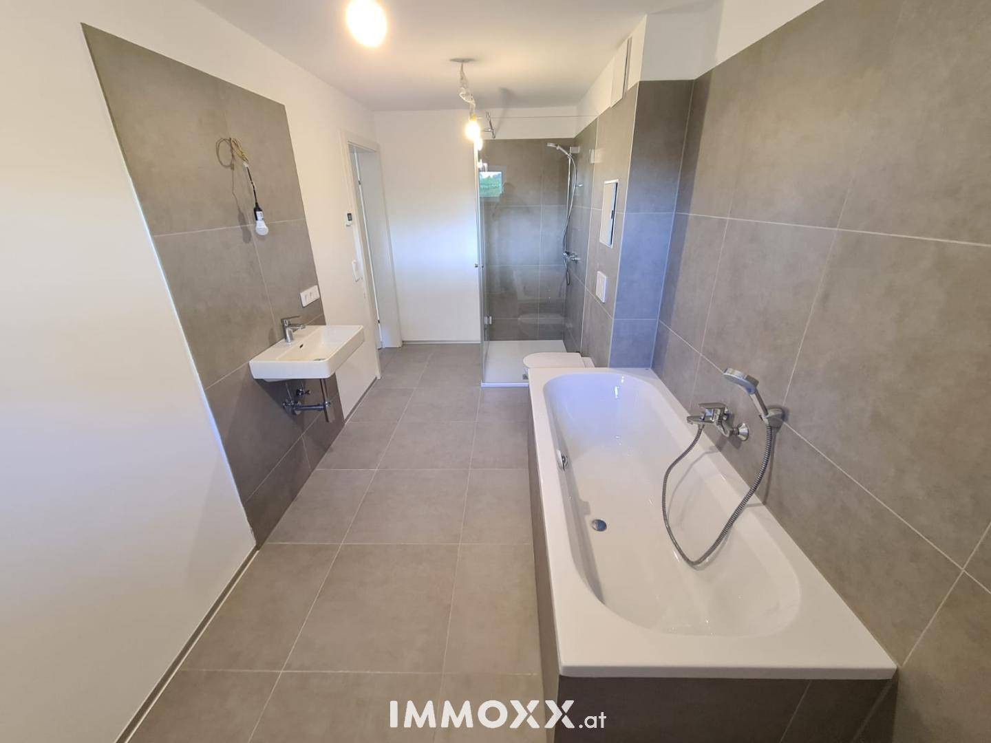 Großes Badezimmer mit Badewanne, separater Dusche und modernen grauen Fliesen.