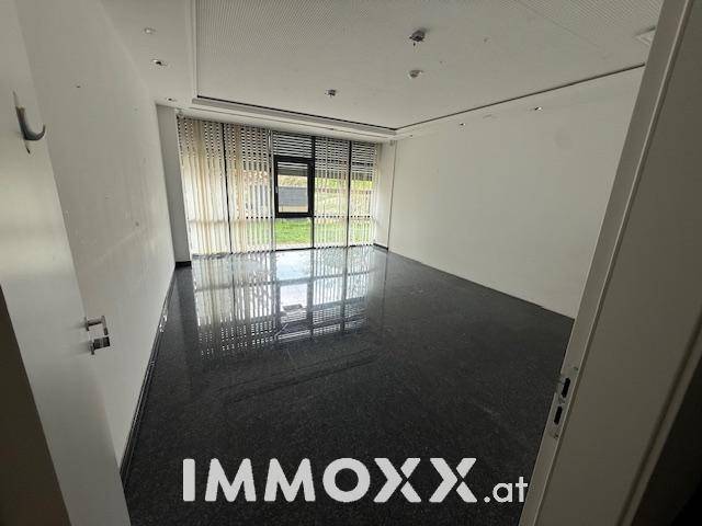 Helles, leeres Büro mit dunklem Steinboden und großen Fenstern mit vertikalen Jalousien.