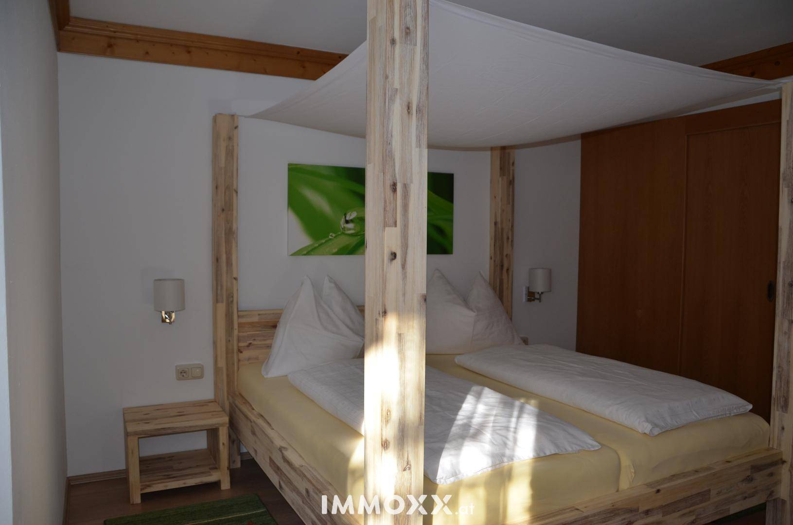 Schlafzimmer mit hellem Holz-Himmelbett, passenden Nachttischen und einem grünen Wandbild.