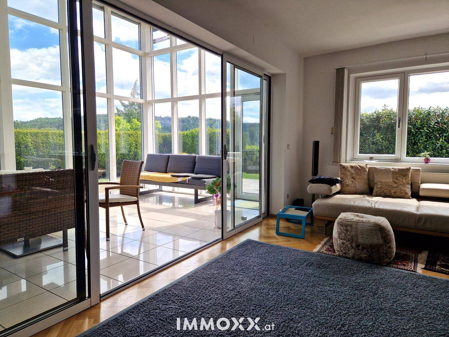 Helles Wohnzimmer mit großen Glasschiebetüren, die zu einem Wintergarten mit Blick ins Grüne führen.