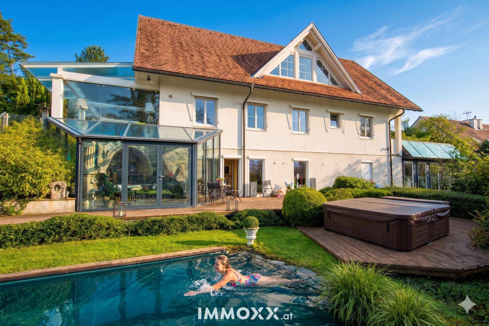 Ansicht des Hauses vom Garten aus mit Pool, Whirlpool auf Holzdeck und verglastem Wintergarten.