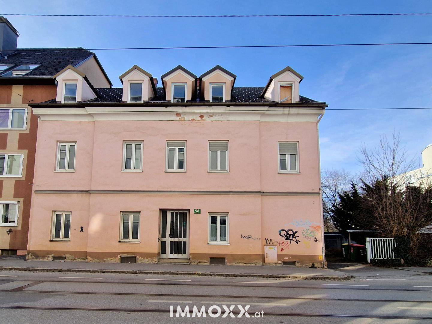 Vorderansicht eines älteren Gebäudes mit rosa Fassade, Dachgauben und Graffiti an der Wand.