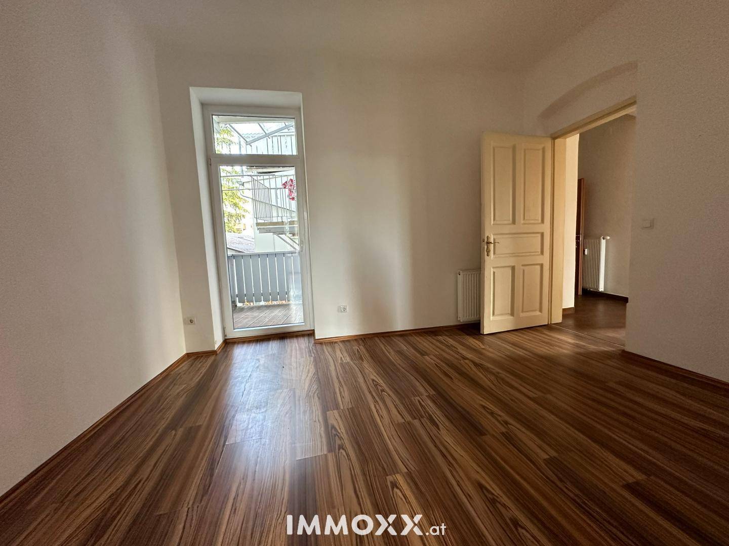 Heller Raum mit Laminatboden, Balkonzugang und einer klassischen Holztür.