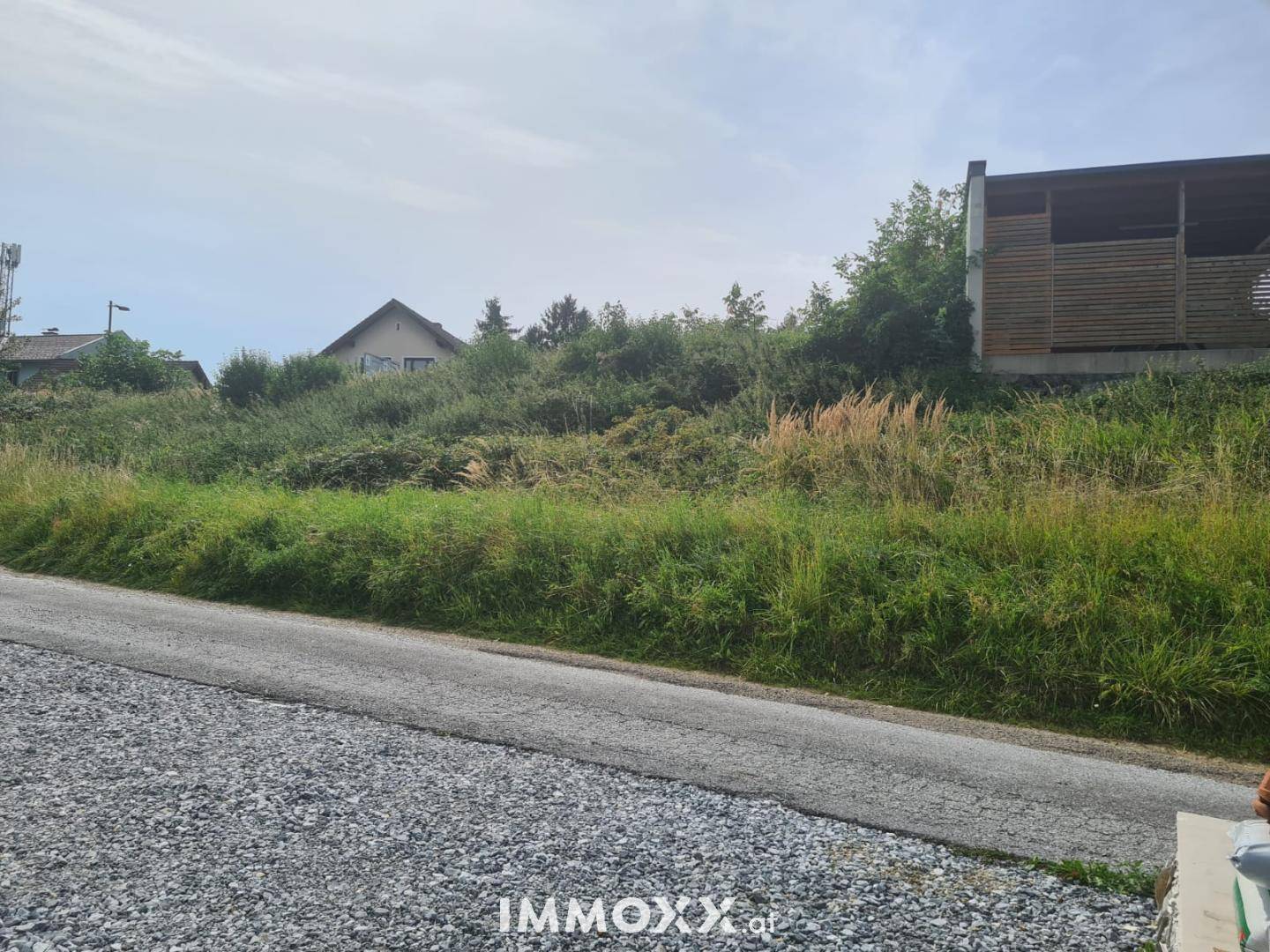 Unbebautes Grundstück mit dichter Vegetation und einer angrenzenden Straße, umgeben von ländlicher Bebauung.