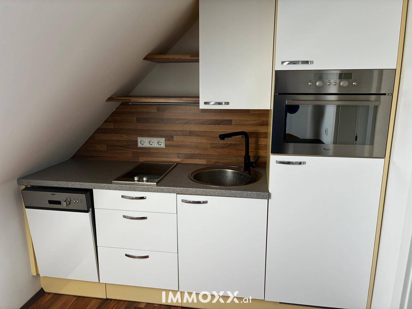 Moderne Küchenzeile im Dachgeschoss mit weißen Schränken, Induktionskochfeld und integriertem Backofen.