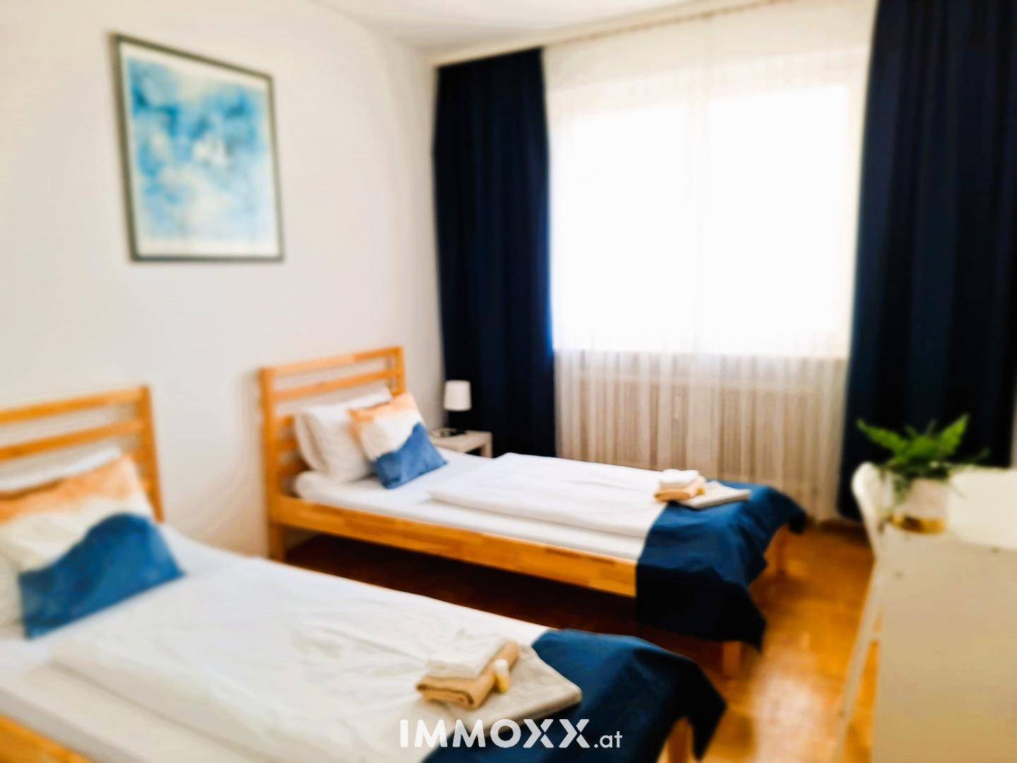 Schlafzimmer mit zwei Einzelbetten, Parkettboden und blauen Vorhängen.