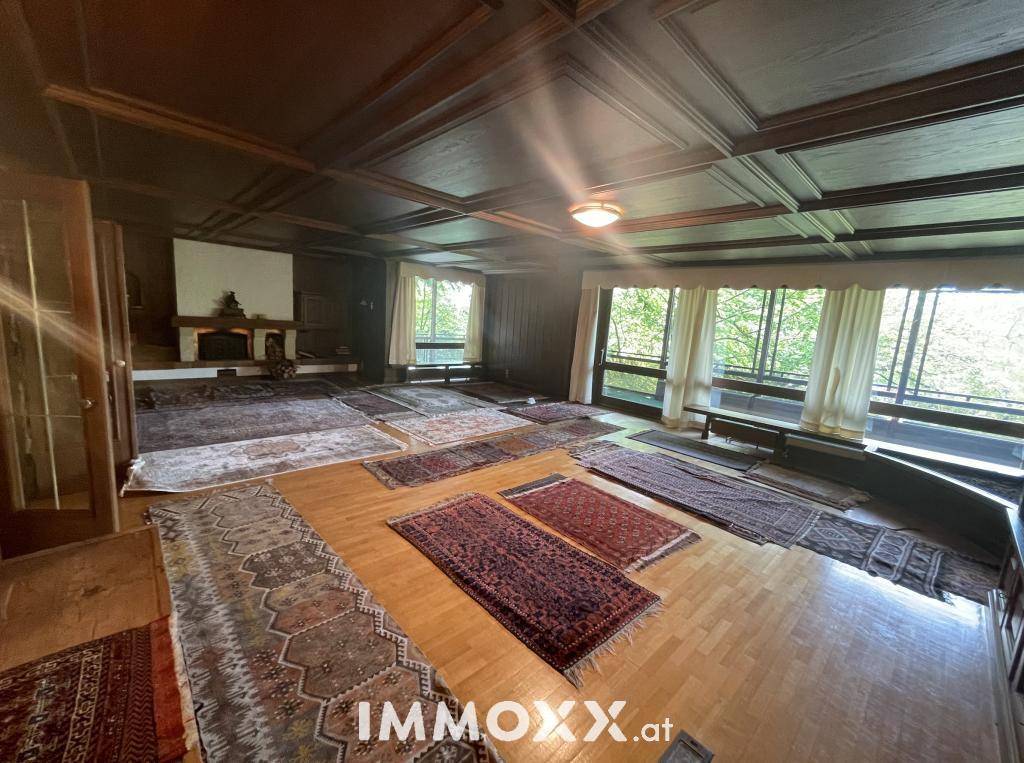 Großzügiges Wohnzimmer mit Parkettboden, Kamin und großen Fenstern mit Blick ins Grüne.