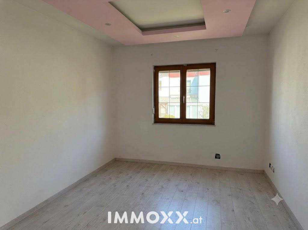 Leeres Schlafzimmer mit hellem Laminatboden und einem Fenster, das viel Tageslicht hereinlässt.