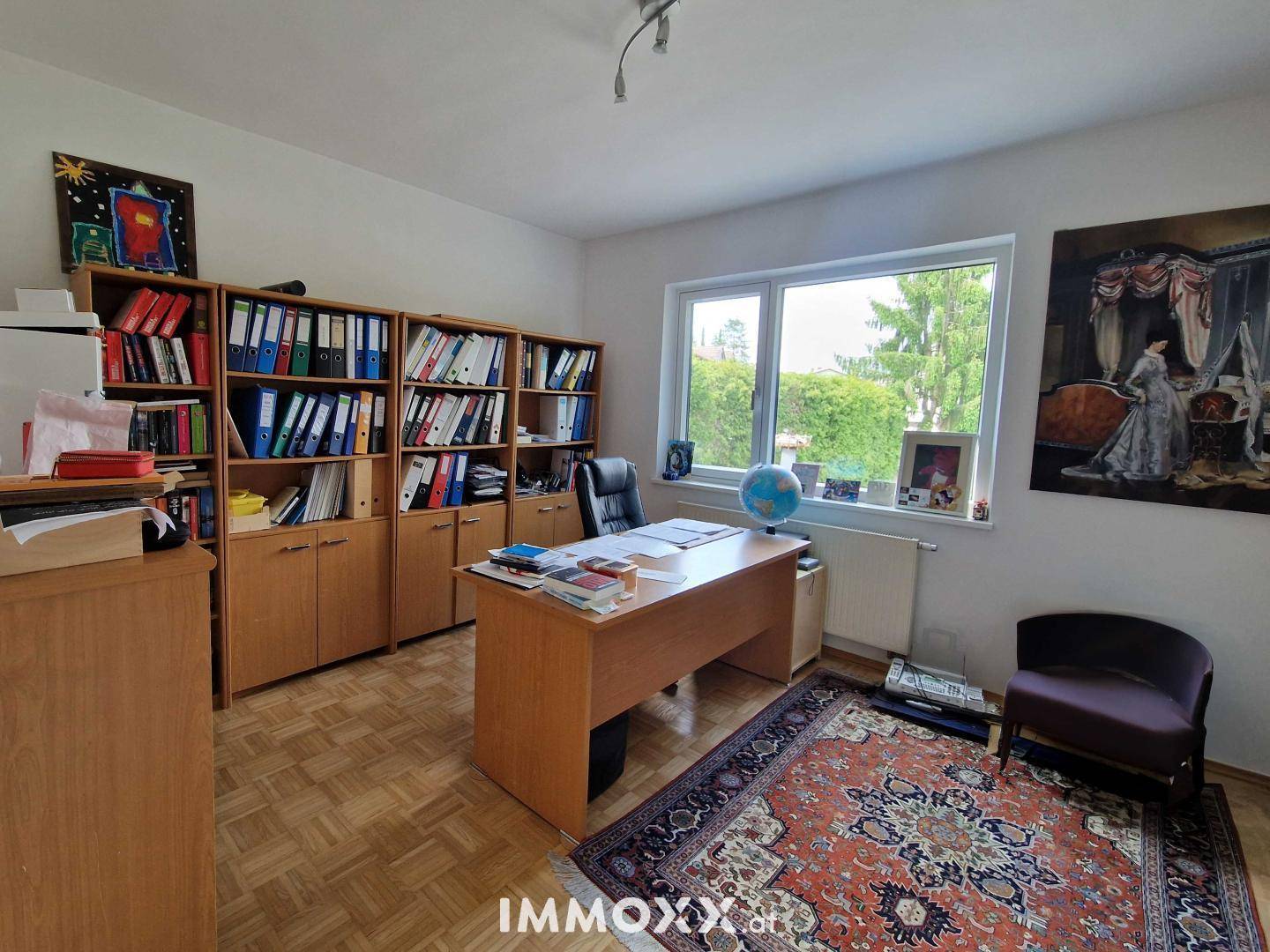 Funktionales Heimbüro mit Holzregalen, Schreibtisch und Fenster mit Blick ins Grüne.