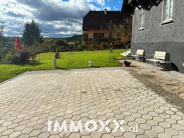 Gepflasterter Außenbereich neben dem Haus mit angrenzender Rasenfläche und Gartenblick.