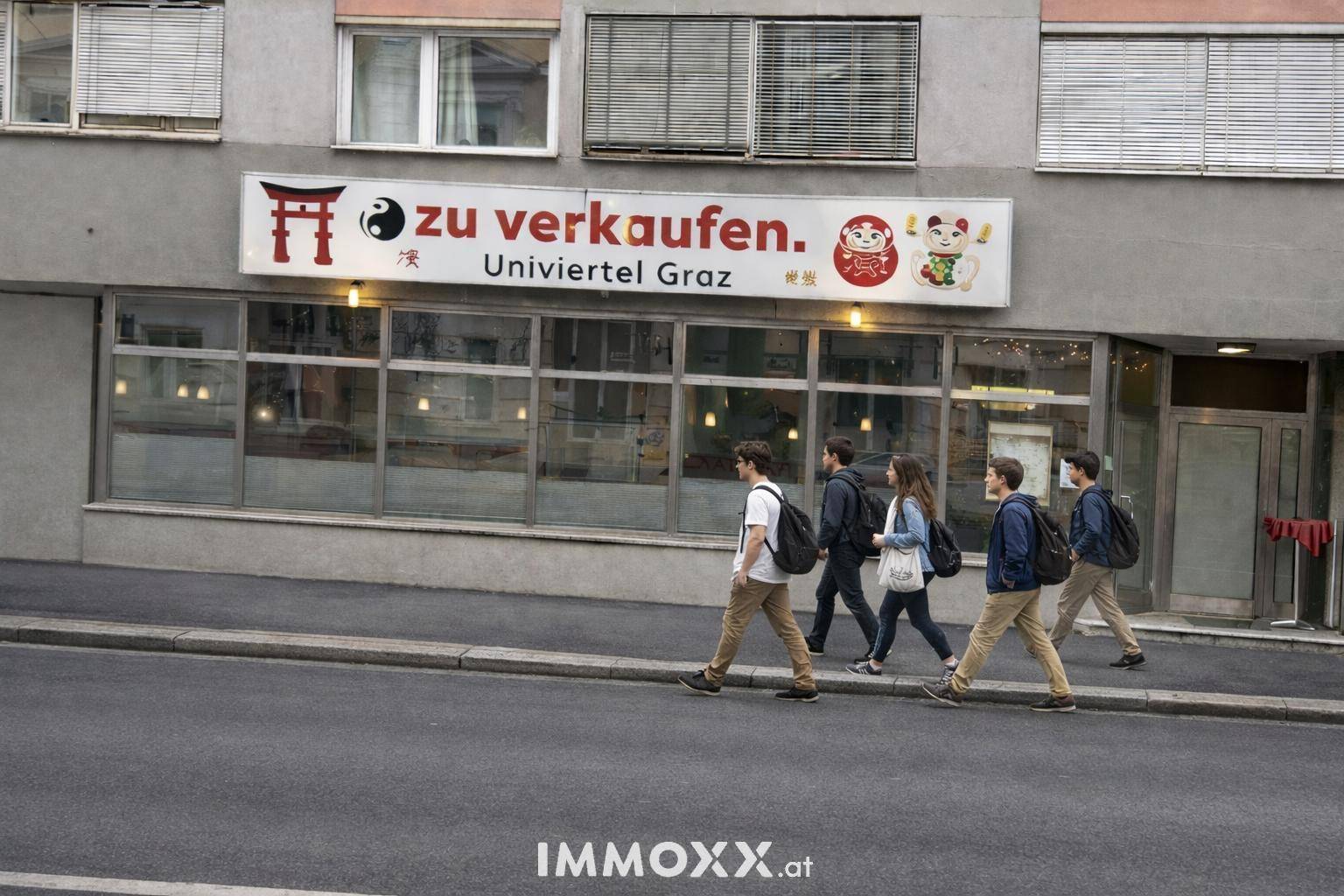 Gebäudefassade mit großen Schaufenstern und einem 'zu verkaufen'-Schild, Passanten gehen auf dem Bürgersteig vorbei.