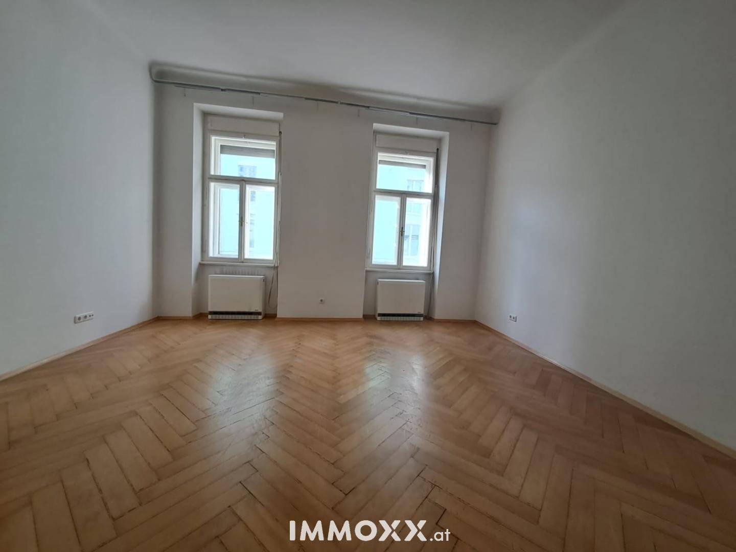 Heller Raum mit Fischgrätparkettboden und zwei großen Fenstern, ideal als Wohn- oder Schlafzimmer.