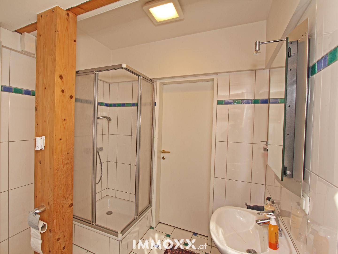 Badezimmer mit Duschkabine, Waschbecken, weißen Fliesen und einem Holzbalken.