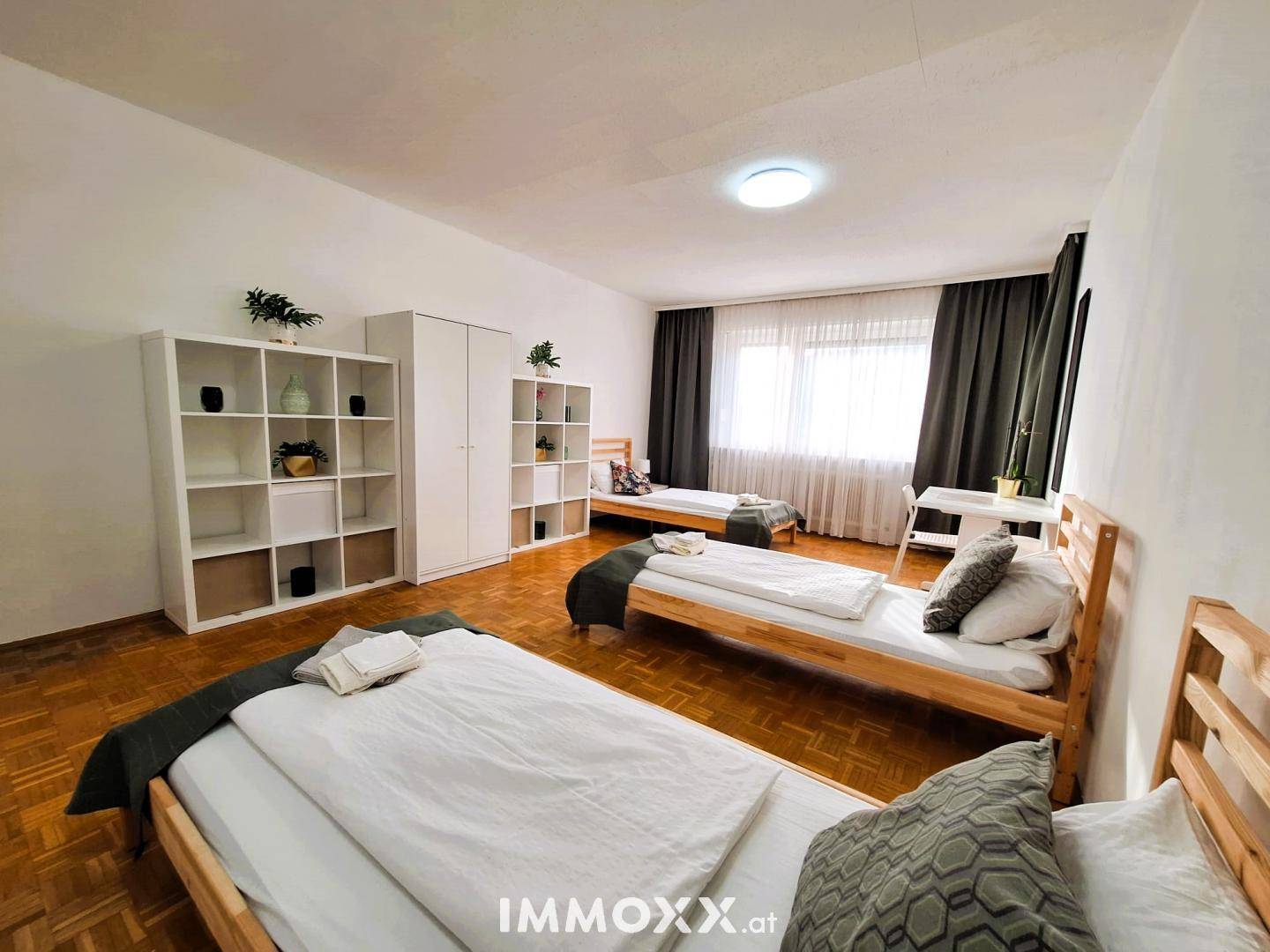Helles Schlafzimmer mit mehreren Einzelbetten, Parkettboden und großem Fenster.