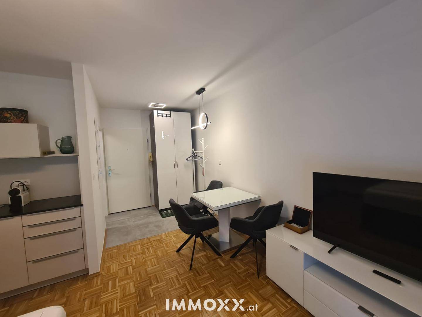 Kompakte Küchenzeile und Essbereich in einem modernen Studio-Apartment mit Parkettboden.