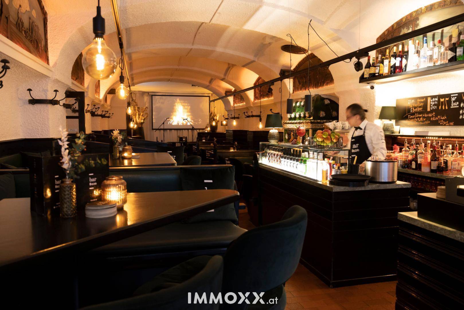 Stimmungsvolle Bar mit gewölbter Decke, dunklen Sitzgelegenheiten und einer Projektion an der Wand.