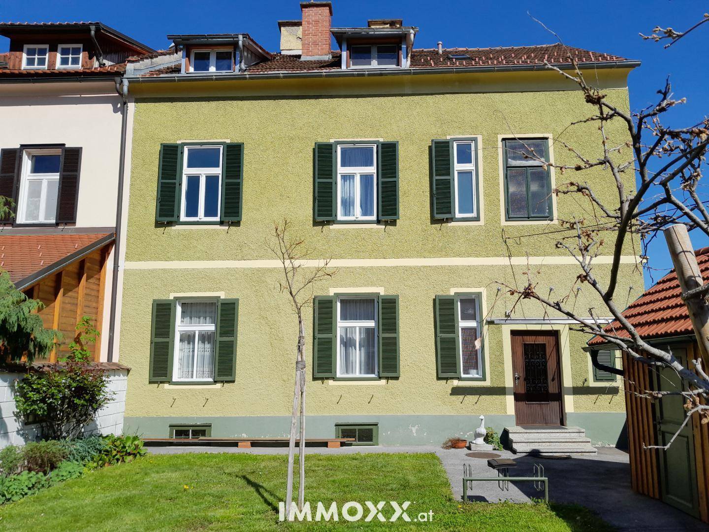 Historisches Wohnhaus mit hellgrüner Fassade, grünen Fensterläden und Vorgarten.