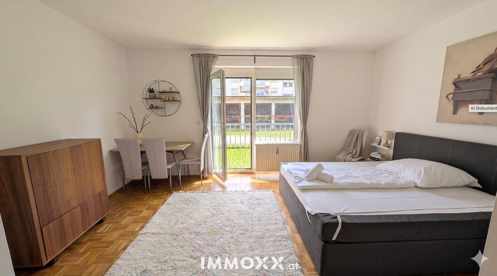 Geräumiges Schlafzimmer mit Parkettboden, Esstisch und Zugang zum Gartenbereich.