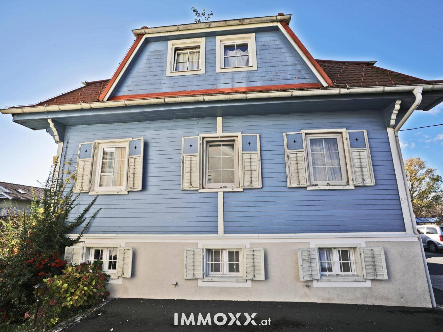 Blaue Holzfassade des Hauses mit Mansarddach und traditionellen Fensterläden.