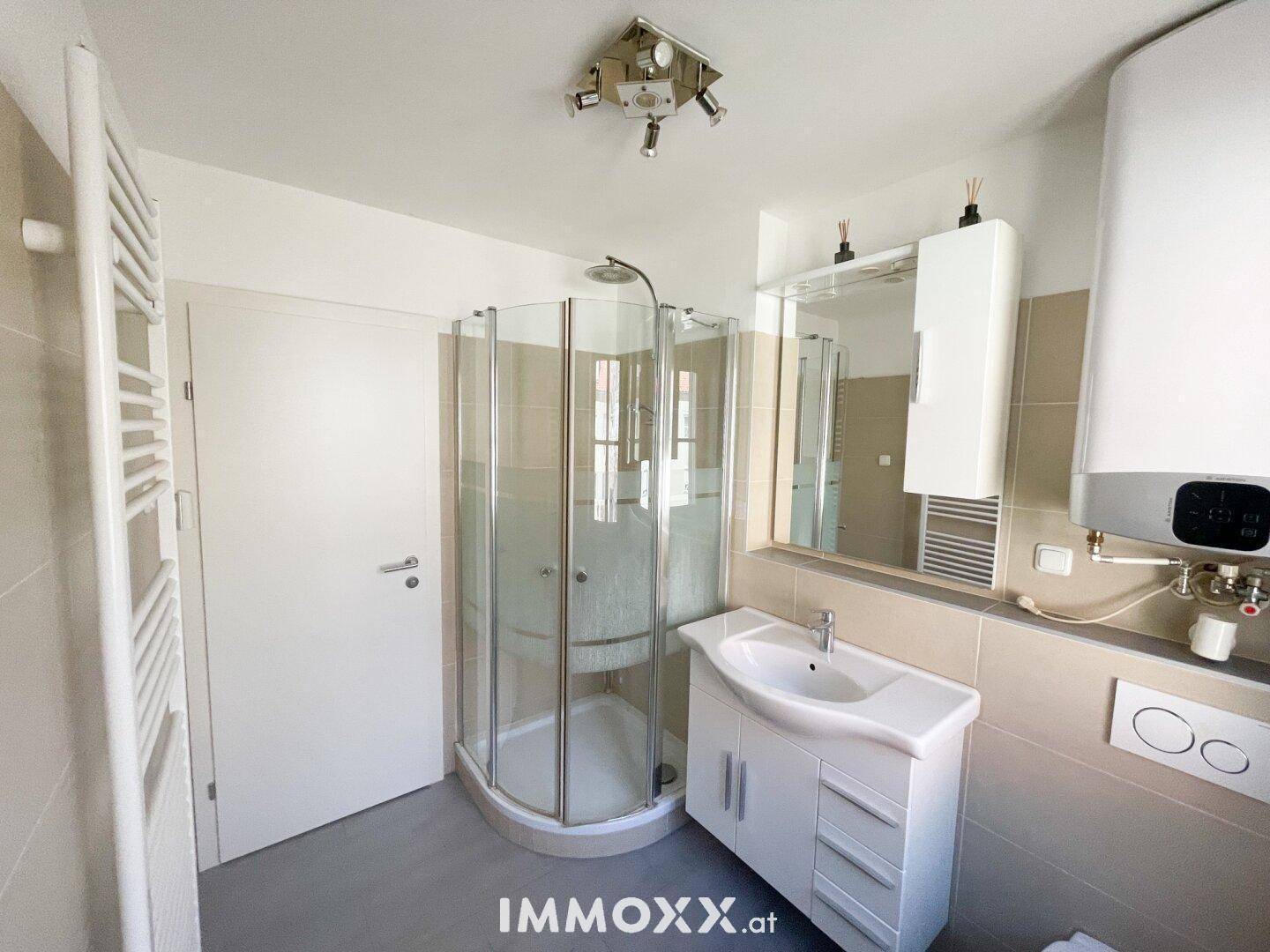 Modernes Badezimmer mit Eckdusche, Waschbeckenunterschrank und beheiztem Handtuchhalter.