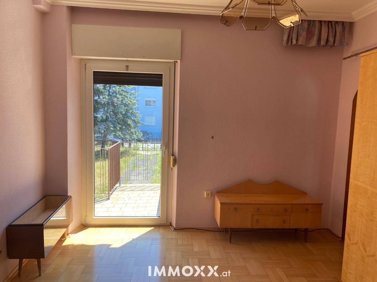 Helles Wohnzimmer mit Parkettboden, lila Wänden und Zugang zu einem Außenbereich.