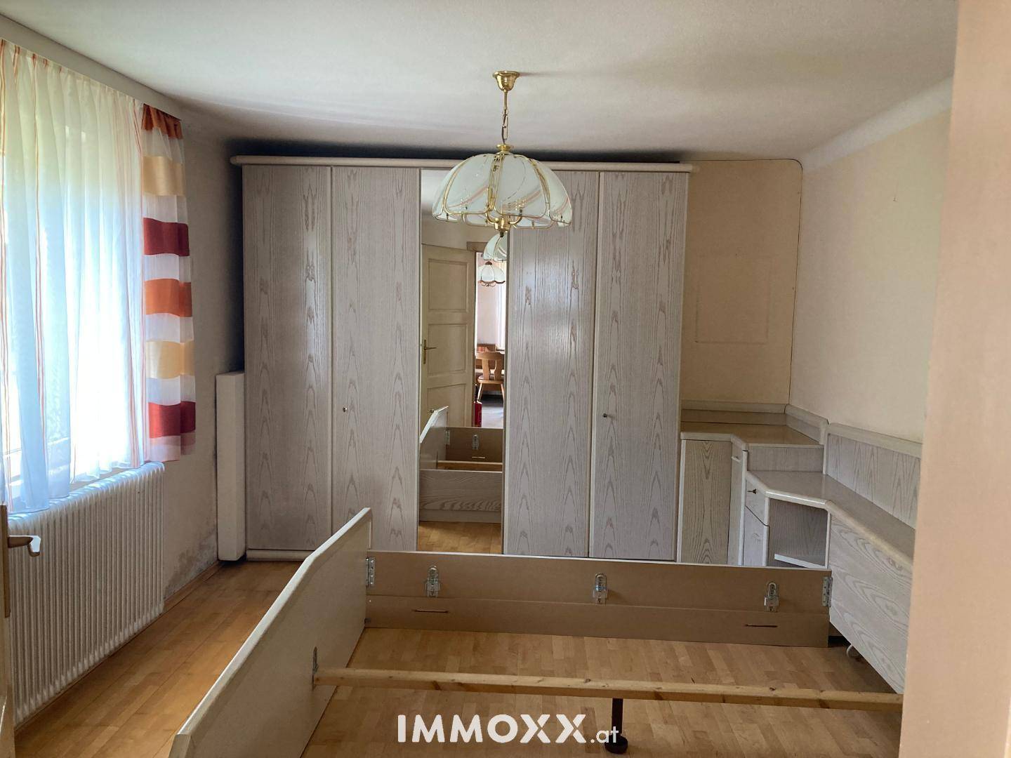Schlafzimmer mit hellem Holzparkett, großem Kleiderschrank und Tageslicht.