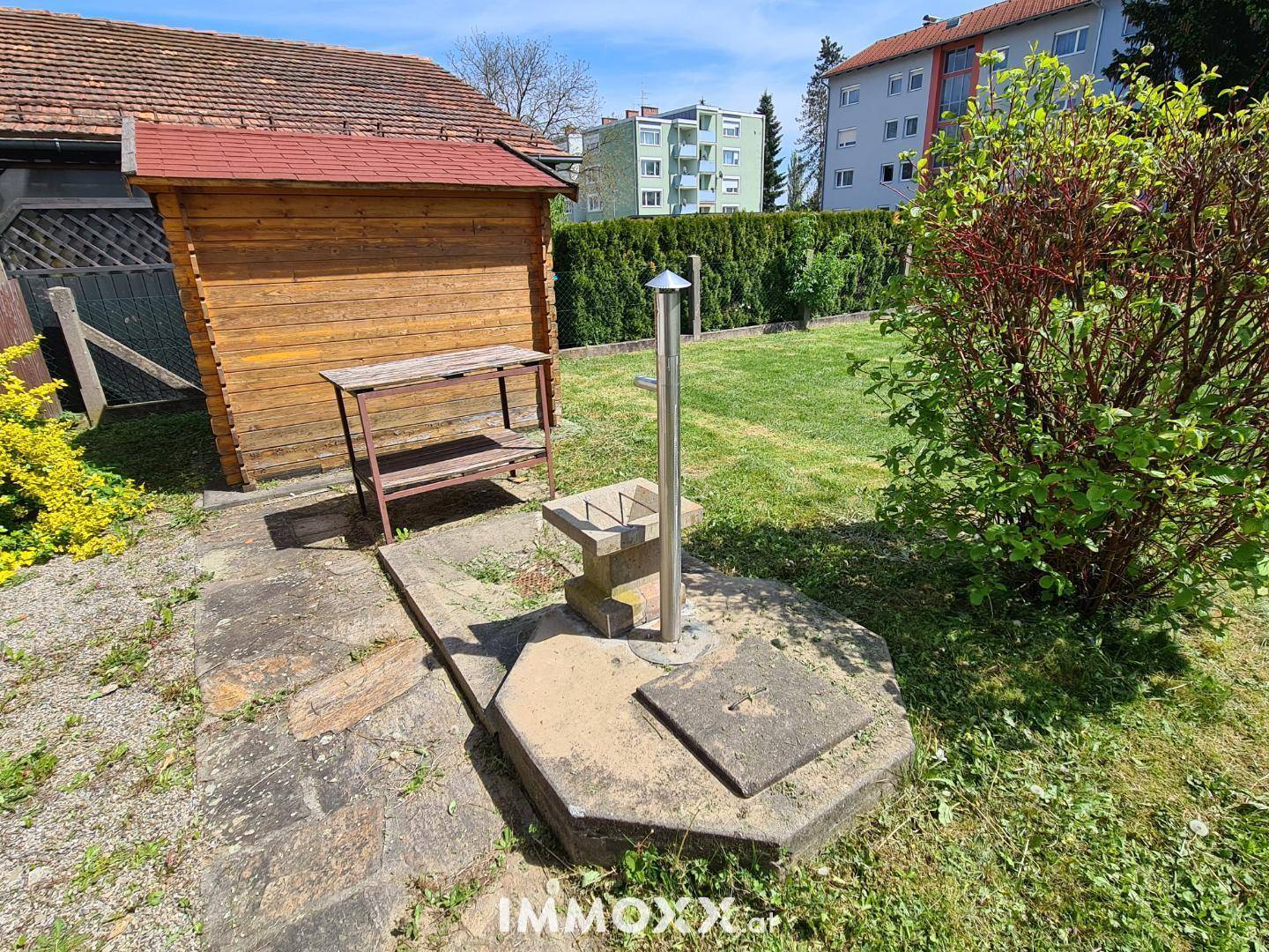 Gartenbereich mit Holzschuppen, Wasserhahn und gepflegter Rasenfläche im Hintergrund.