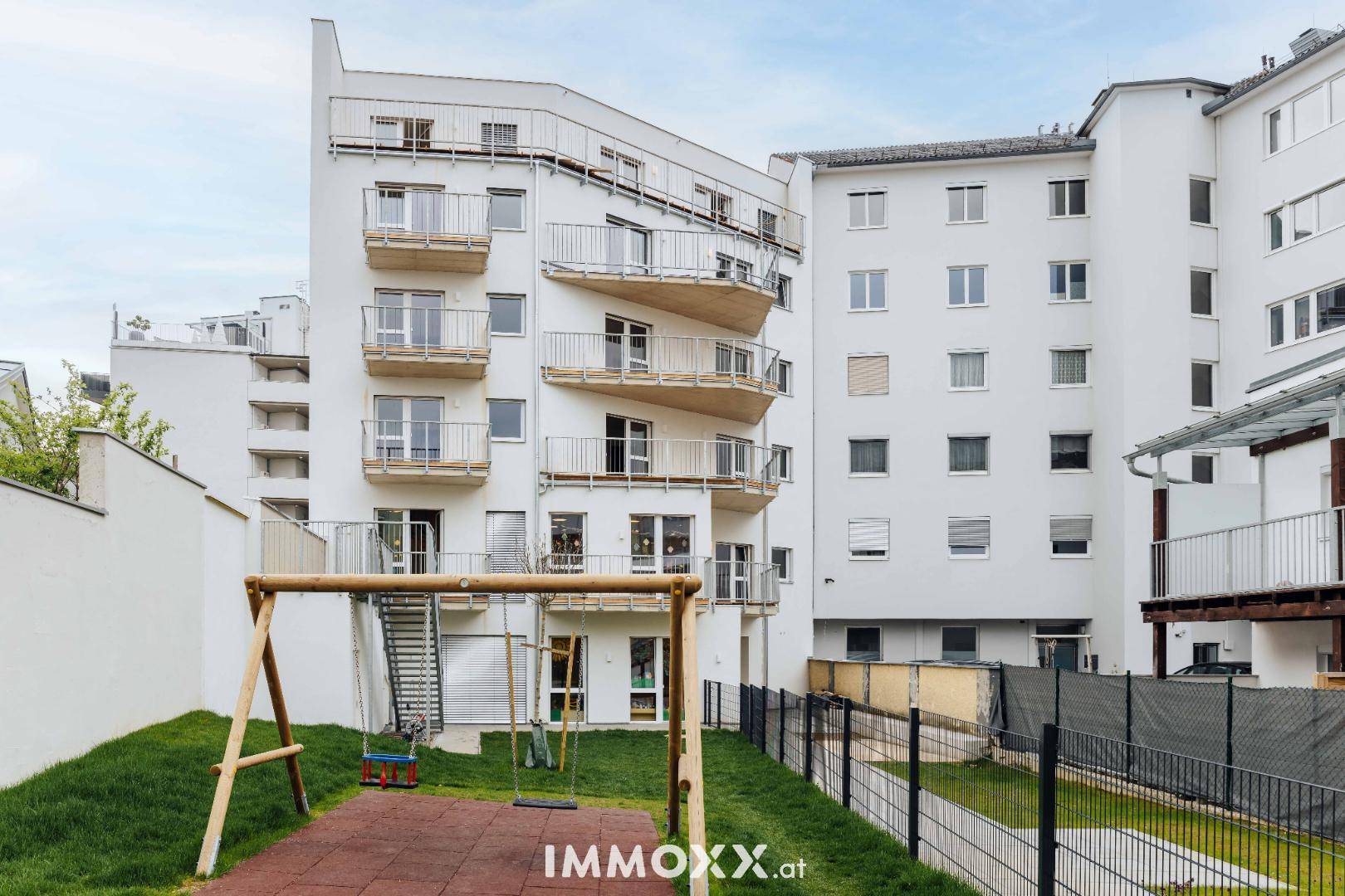 Moderne Wohnanlage mit weißen Fassaden, Balkonen und einem Kinderspielplatz im Freien.