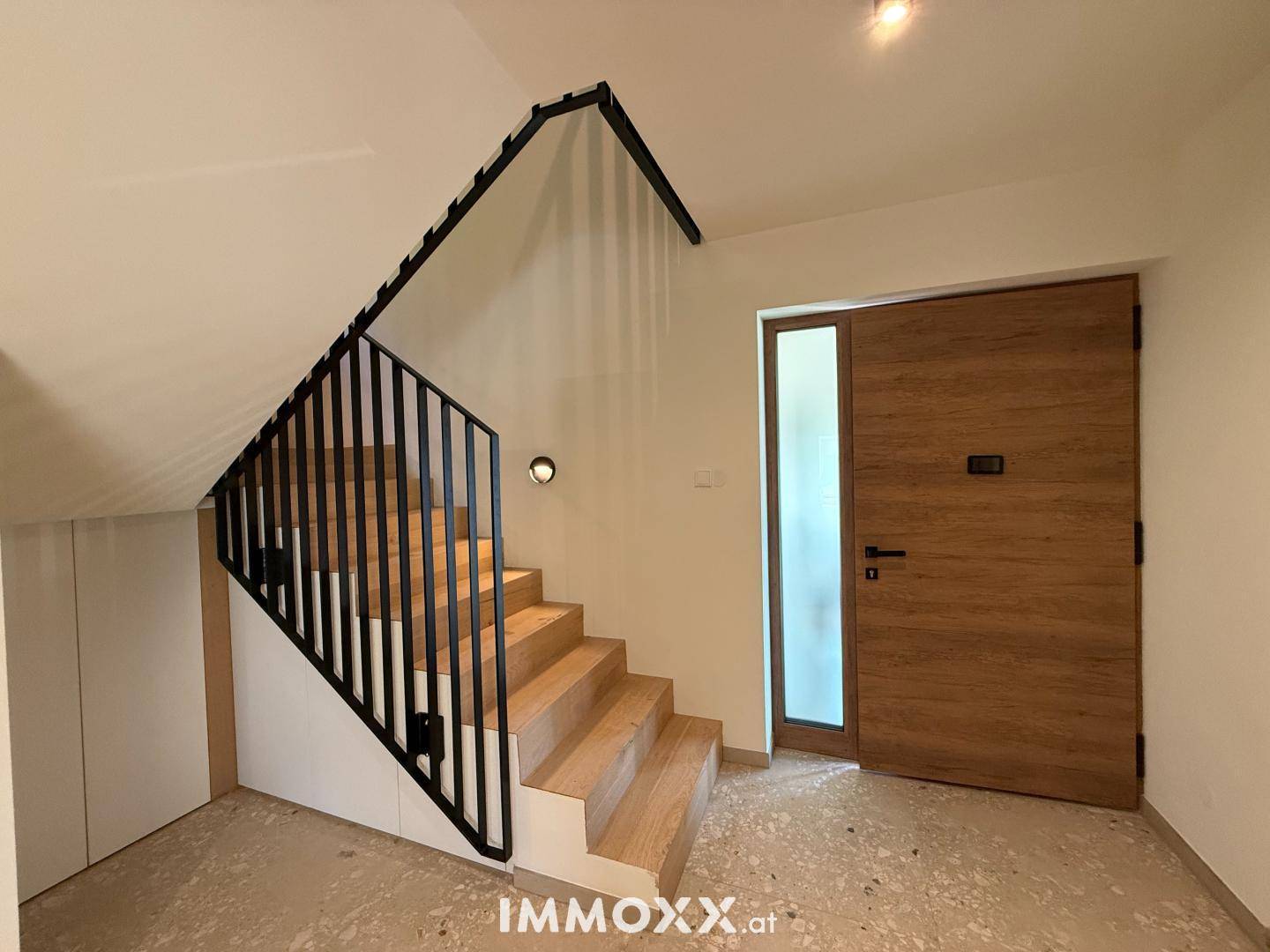 Heller Flur mit moderner Holztreppe und stilvoller Eingangstür mit seitlichem Glaselement.